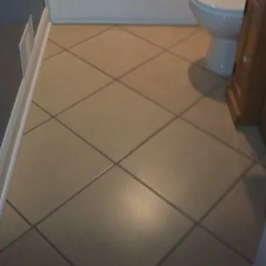 Diagonal beige tile flooring beside a bathroom vanity and toilet